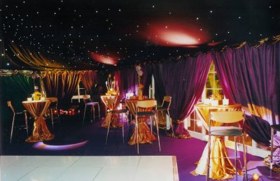 50th Private Party Decor with purple drapery, golden high pod table linen and a star like marquee ceiling