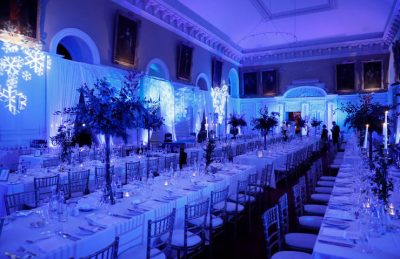 corporate christmas dinner at the RHK in Dublin with long trestle tables, golden candelabras, christmas green centre pieces, white drapery and soft blue lightning with snow flakes projectors